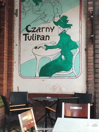 Brama i ogródek — Latem stoliki na zewnątrz, pod muralem z tulipanową damą.