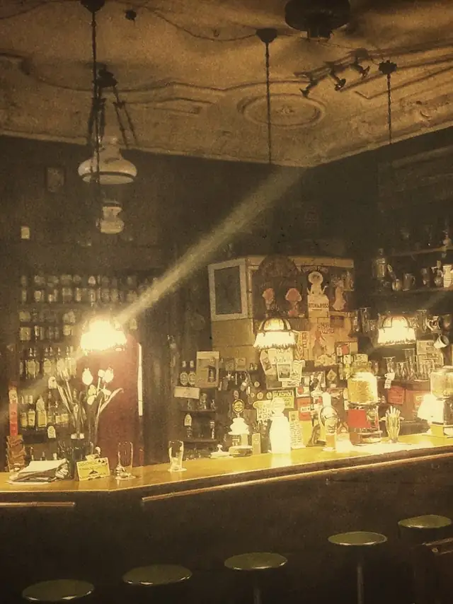 Bar Czarnego Tulipana w ciepłym świetle lamp, półki z butelkami i stołki barowe